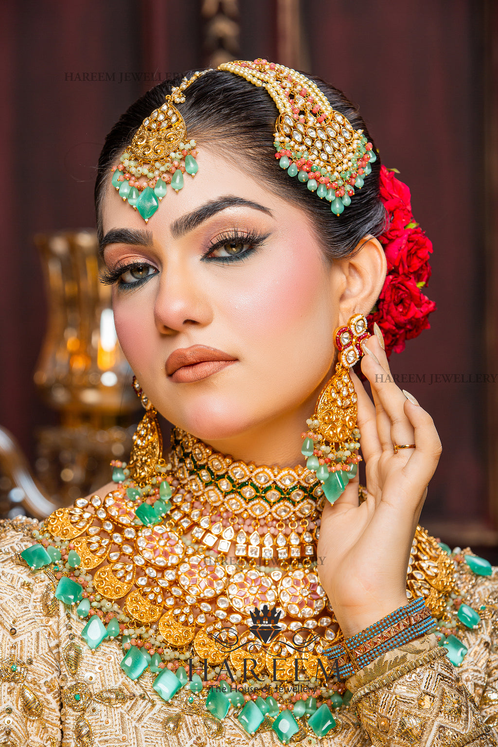 Woman wearing elaborate gold jewelry with green stones against a blurred background