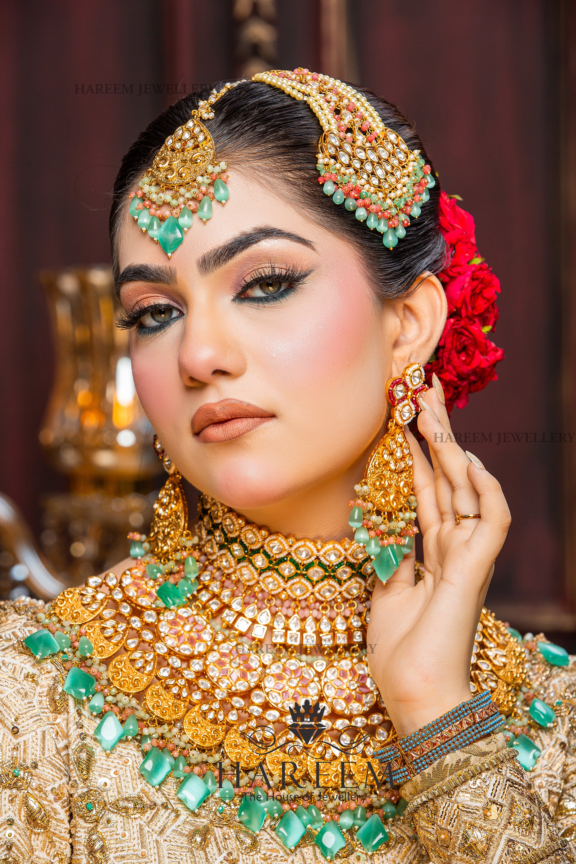 Woman wearing elaborate gold jewelry with green stones against a blurred background