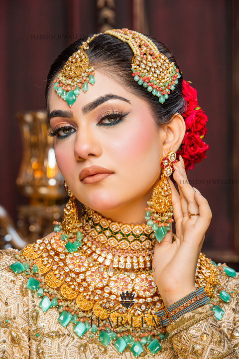Woman wearing elaborate gold jewelry with green stones against a blurred background